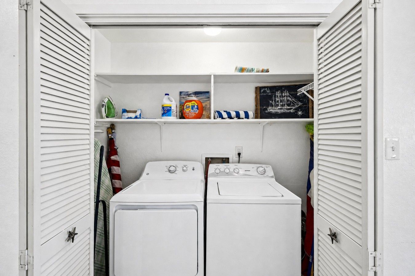 A laundry room with two front-loading washing machines, shelves with laundry supplies, and a chalkboard with a drawing.