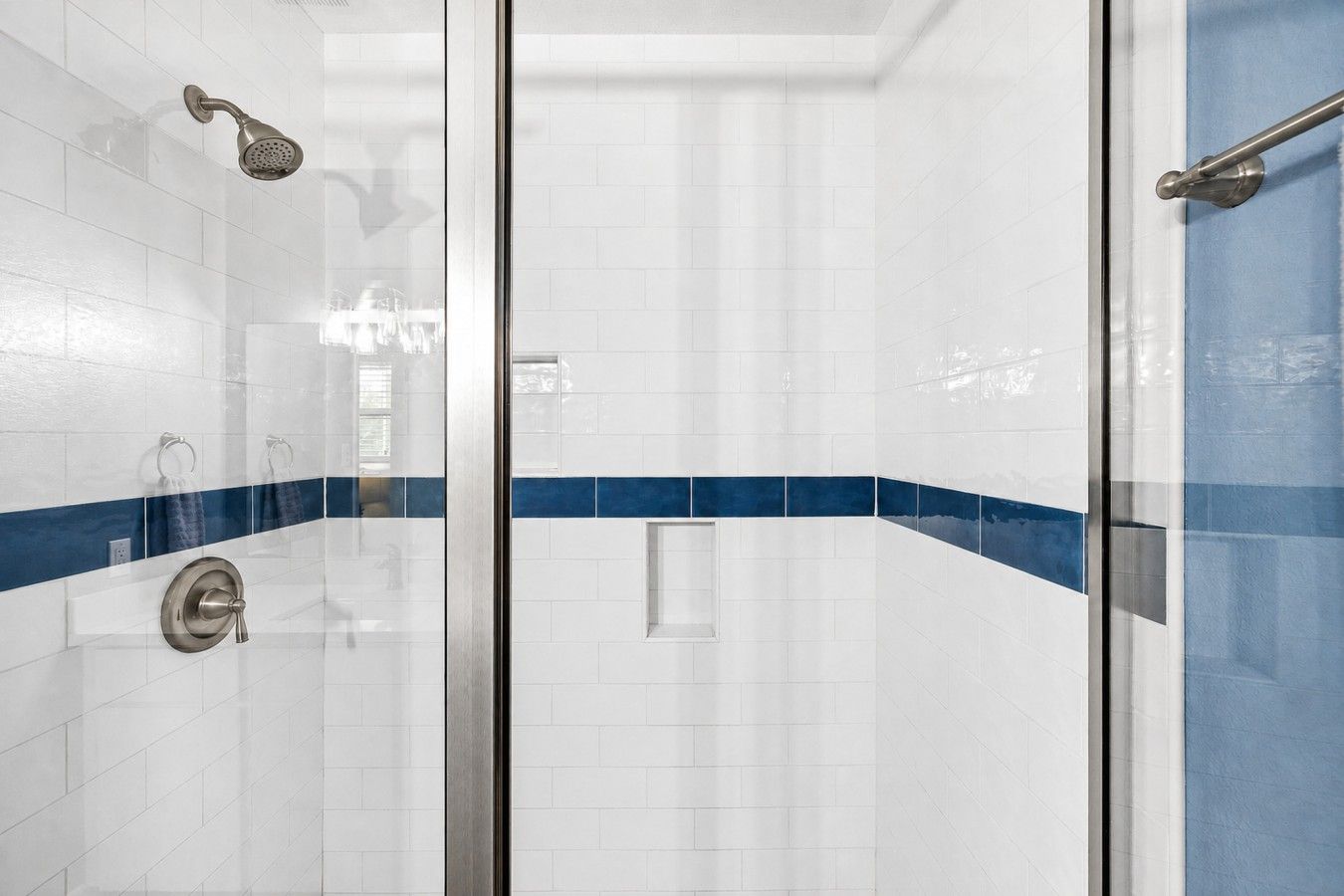 A glass-enclosed shower with a handheld showerhead and a wall-mounted control valve.