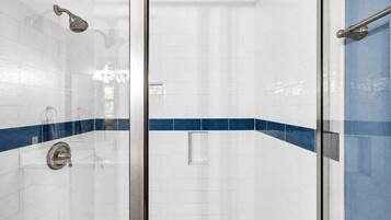 A glass-enclosed shower with a handheld showerhead and a wall-mounted control valve.