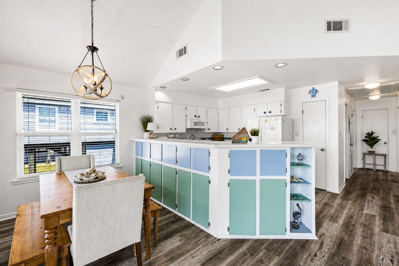 A modern kitchen with a central island, white cabinetry, and a wooden dining table.