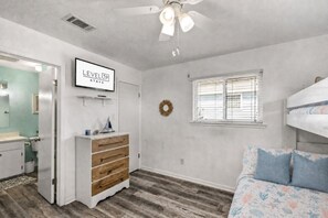 Un dormitorio con literas, cómoda, tocador con espejo, ventilador de techo y televisor montado en la pared.