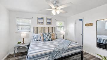 Un dormitorio con cama, mesitas de noche, ventilador de techo y un espejo grande.