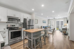 A modern kitchen with stainless steel appliances, a wooden dining table, and a view to a balcony. - Private Beach, Heated Pool, Hot Tub, Pickleball (Gulf Shores)