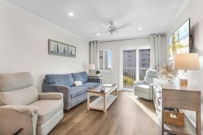 A living room with a sofa, a coffee table, a lamp, and a view of the outside. - Private Beach, Heated Pool, Hot Tub, Pickleball (Gulf Shores)