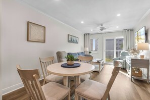 A dining area with a round table, chairs, and a central plant. There is a sofa and a television in the background. - Private Beach, Heated Pool, Hot Tub, Pickleball (Gulf Shores)