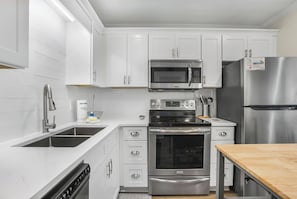 A modern kitchen with white cabinets, stainless steel appliances, and a wooden countertop. - Private Beach, Heated Pool, Hot Tub, Pickleball (Gulf Shores)