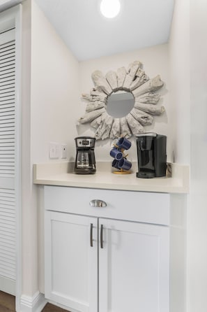 A kitchen with a white countertop, a coffee maker, a coffee pot, and a decorative mirror. - Private Beach, Heated Pool, Hot Tub, Pickleball (Gulf Shores)
