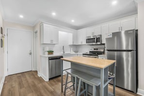 A modern kitchen with white cabinets, stainless steel appliances, a wooden countertop, and bar stools. - Private Beach, Heated Pool, Hot Tub, Pickleball (Gulf Shores)
