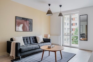 A modern living room with a grey sofa, a round coffee table, and a large window offering a view of buildings. - Blueground | Nusle, balcony, well-connected, cafes (PRG-77) (Prague)