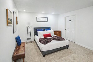 Ein Schlafzimmer mit einem Bett, einem Nachttisch, einer Lampe, einer Bank und einer Tür.