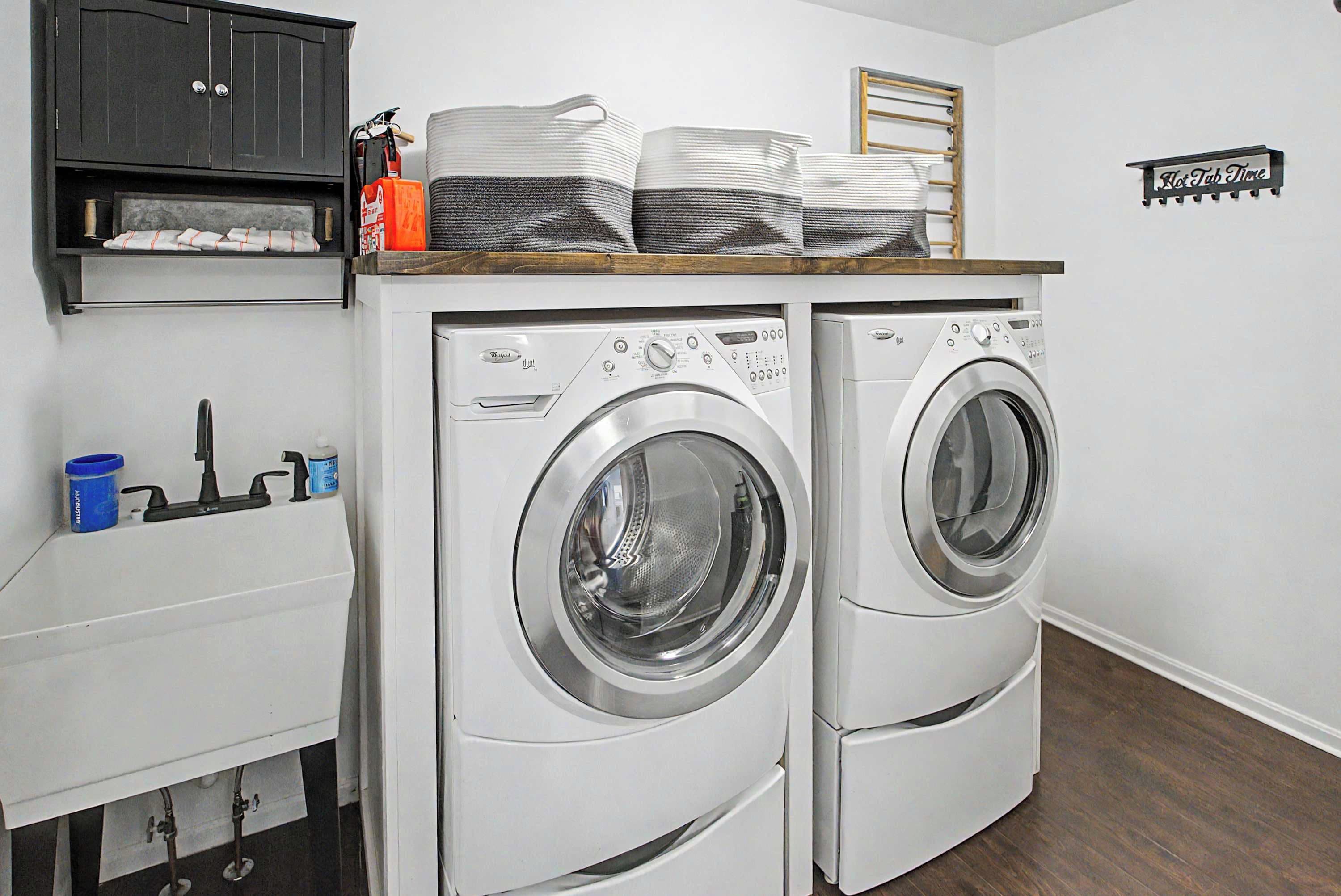 A laundry area with two front-loading washing machines, a cabinet above, and a small sink with a blue container.