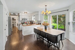 A modern kitchen with white cabinetry, a central island, and a dining area with black chairs. - Taste of Home - Erlanger (Erlanger)