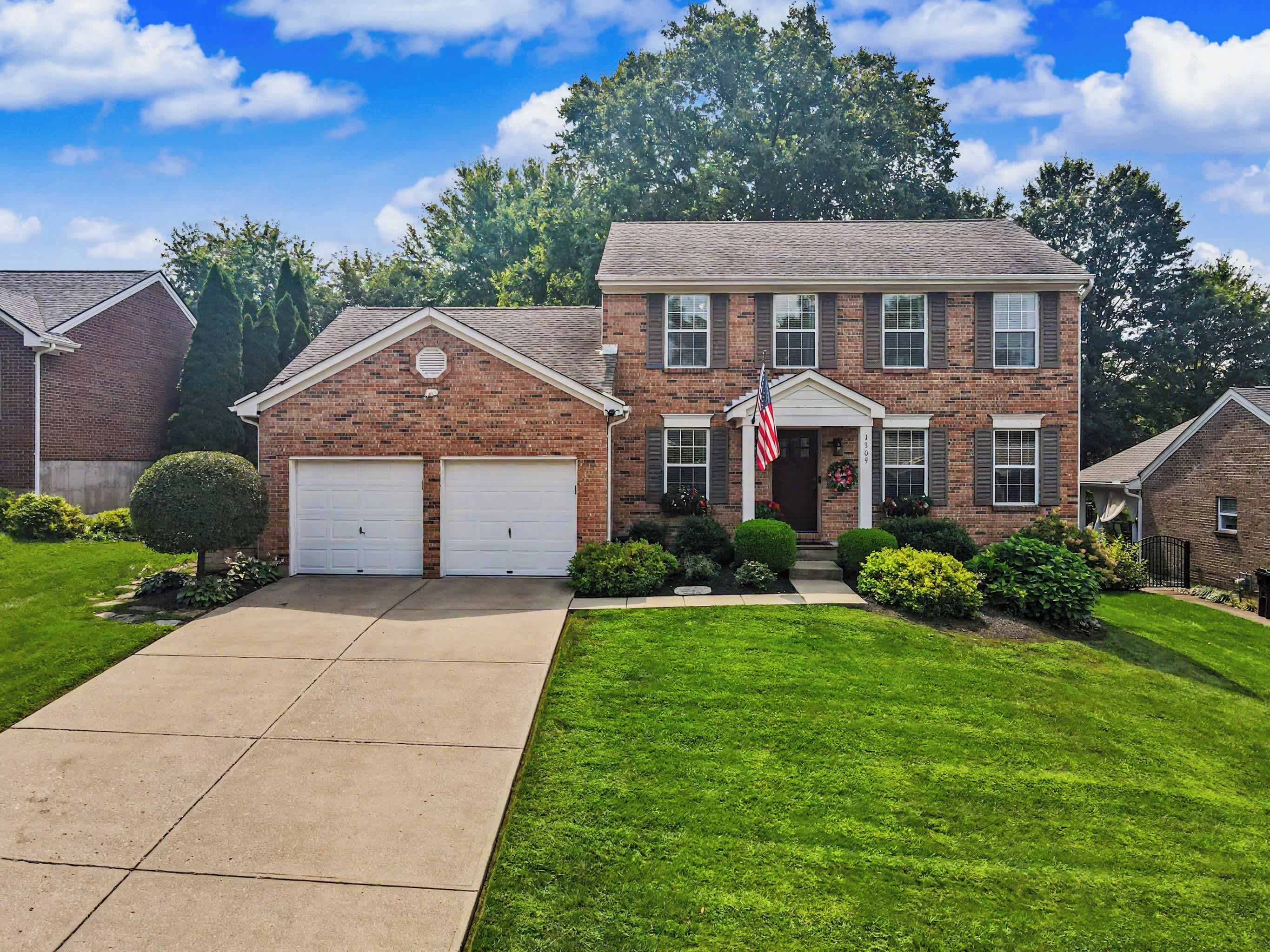 A two-story brick house with a front garage, a well-maintained lawn, and a flag.