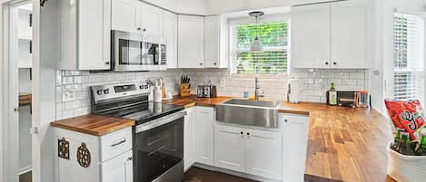 A modern kitchen with white cabinets, a stainless steel oven, a microwave, and a wooden countertop.