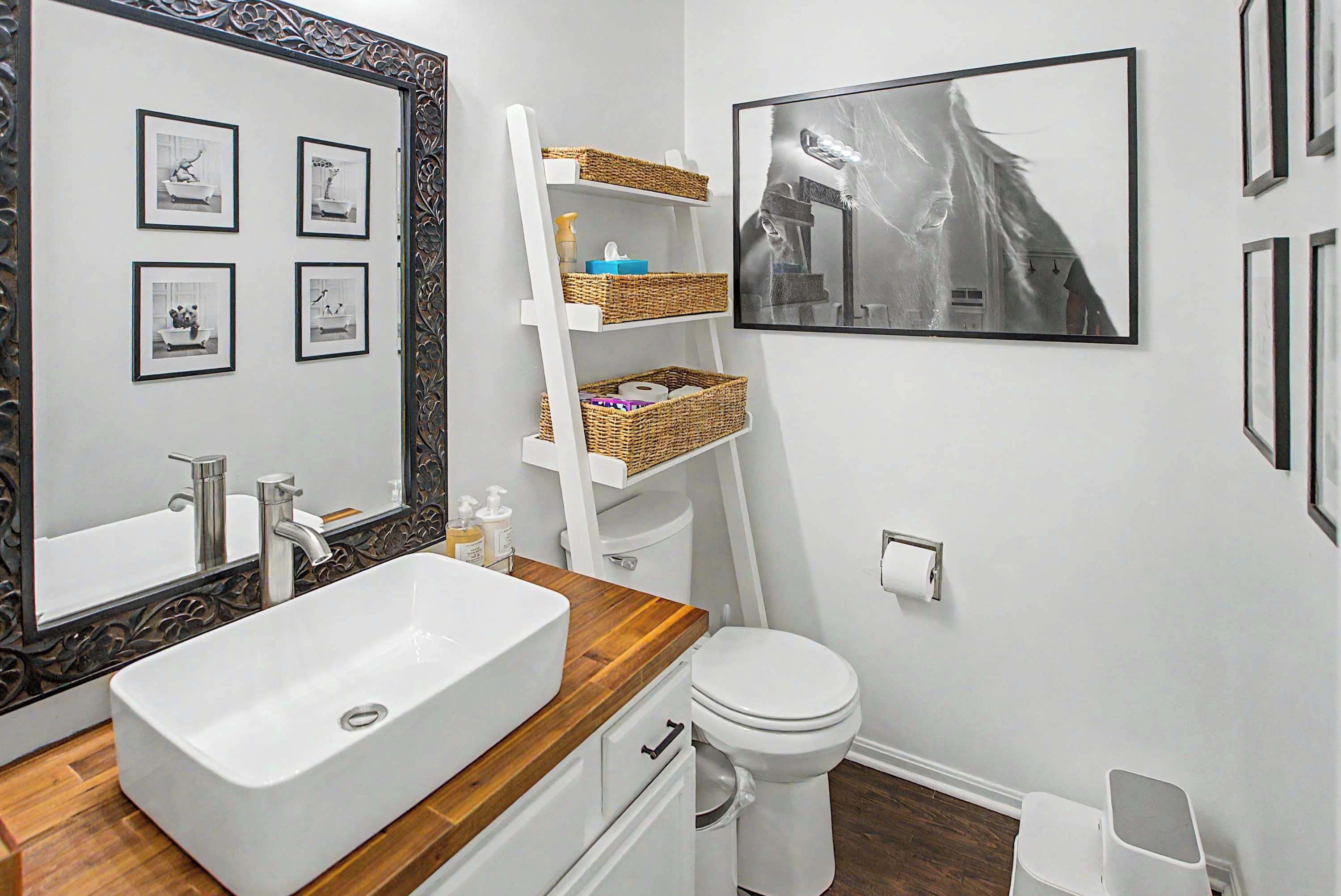 Une salle de bain avec un grand miroir, un lavabo blanc, des toilettes et des tableaux encadrés accrochés au mur.