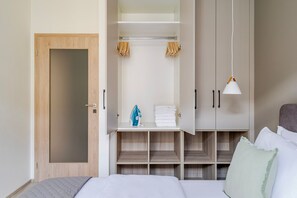 Ein Hotelzimmer mit einem Bett, einem Kleiderschrank mit Kleidung und einer Ablage mit Handtüchern und einer Tasche.