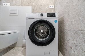 Eine Waschmaschine mit Frontlader, einer Bedienblende, einer Steckdose und einem an der Wand montierten Lichtschalter.