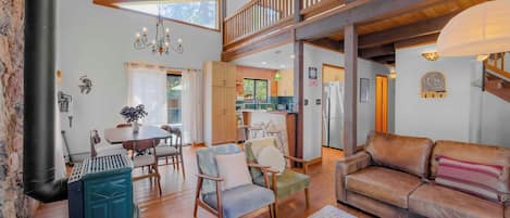 A spacious living area with a high ceiling, wooden beams, a dining table with chairs, a sofa, and a fireplace.