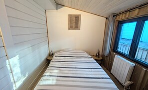 Et soveværelse med seng, et vindue, en radiator og en ventil i væggen.