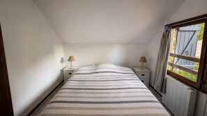 Una habitación pequeña con una cama, dos mesitas de noche y un ventanal con cortinas.