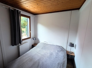 Et soveværelse med seng, et vindue med gardiner, en radiator og et natbord med lampe.