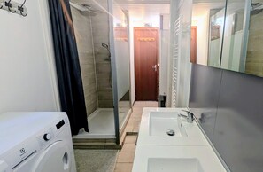 Un baño pequeño con ducha, lavamanos y lavadora.