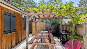 En træpergola med et bord og stole under, omgivet af et træhegn og en murstensmur.