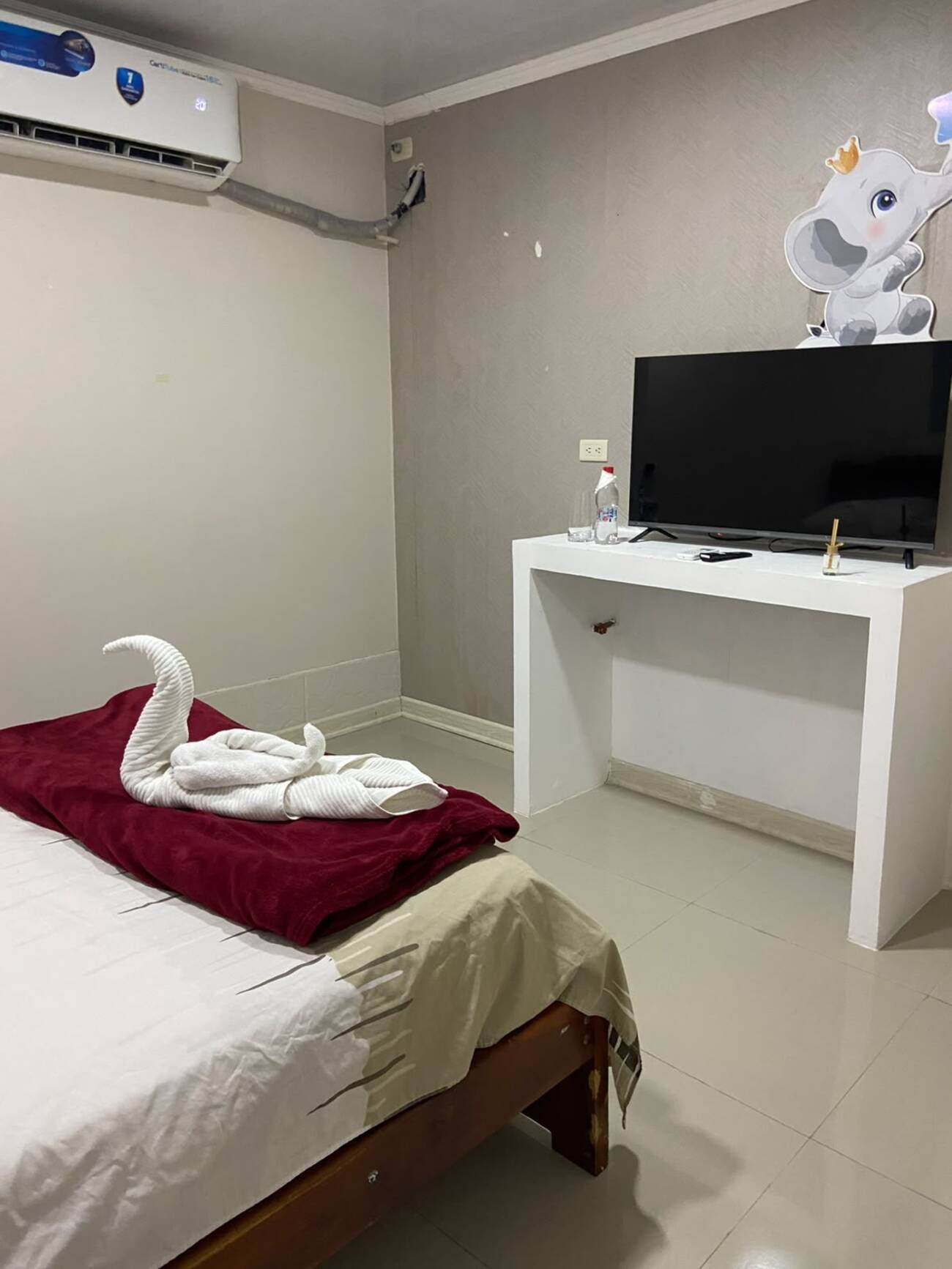 A hotel room with a bed, a TV on a white desk, and a wall decoration.