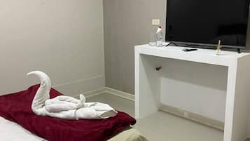 A hotel room with a bed, a TV on a white desk, and a wall decoration.