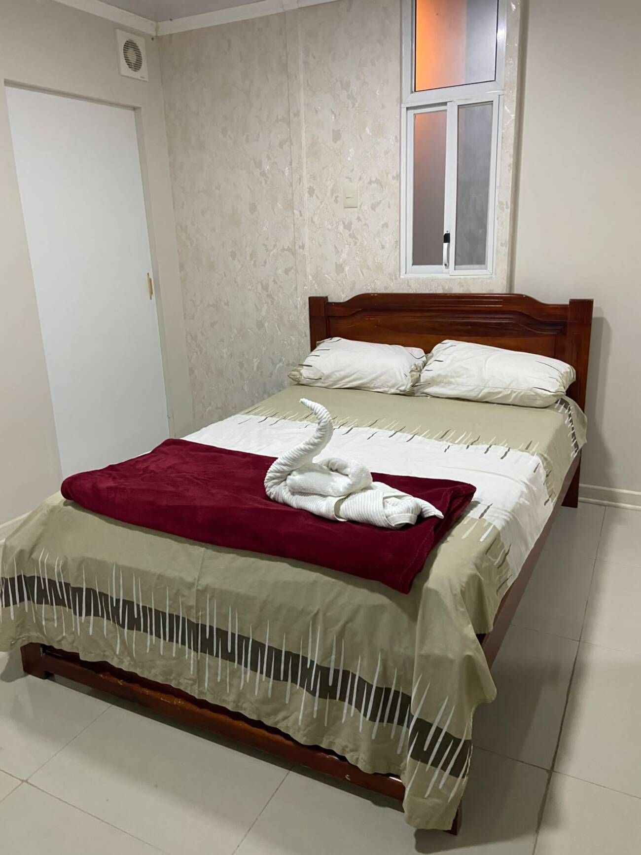 A bed with a wooden headboard, white bedding, a red throw blanket, and a white towel arranged on the bed.