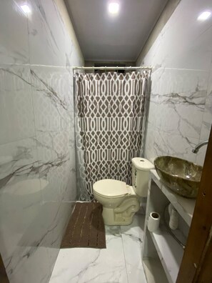 Een badkamer met een toilet, een wastafel met een grote wasbak en een douchegordijn met een geometrisch patroon.