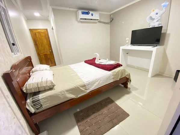Een slaapkamer met een bed, een televisie op een standaard, een airconditioning en een deur.