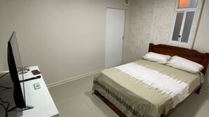 Quarto com cama, escrivaninha, computador, janela e porta.