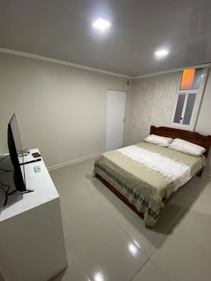 Een slaapkamer met een bed, een bureau met een computer, een raam en een deur.