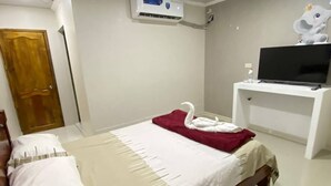 Quarto com cama, televisão em móvel, aparelho de ar condicionado e porta.