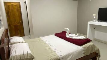 A hotel room with a bed, a wooden door, a white wall, and a white air conditioning unit.