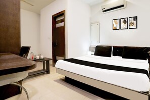 A hotel room with a bed, a desk, a chair, a wardrobe, and a mirror.