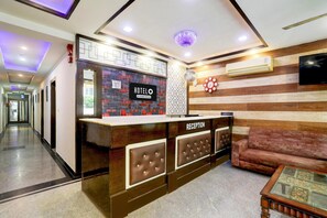 A hotel reception area with a reception desk, a sofa, a TV, and a patterned wall.