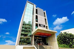 A modern hotel with a glass facade, a visible reception area, and a staircase leading to the entrance.