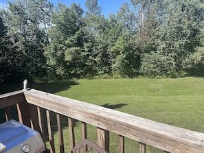 A wooden deck with a grill and a view of a grassy yard and trees. - Sunny, Quiet Condo on Golf Course near Mount Snow and Hermitage Resorts (Wilmington)