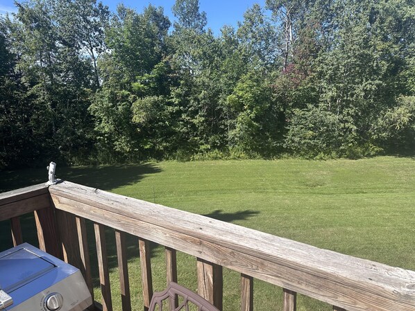 A wooden deck with a grill and a view of a grassy yard and trees.