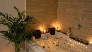 A spa room with a large bathtub, candles, and a potted plant.