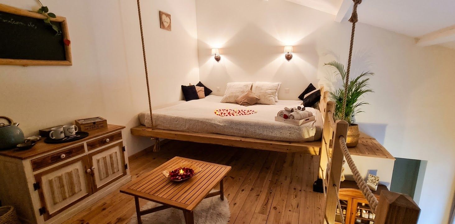 Un dormitorio acogedor con una cama suspendida, lámparas de noche, un aparador de madera y una mesita con una vela.