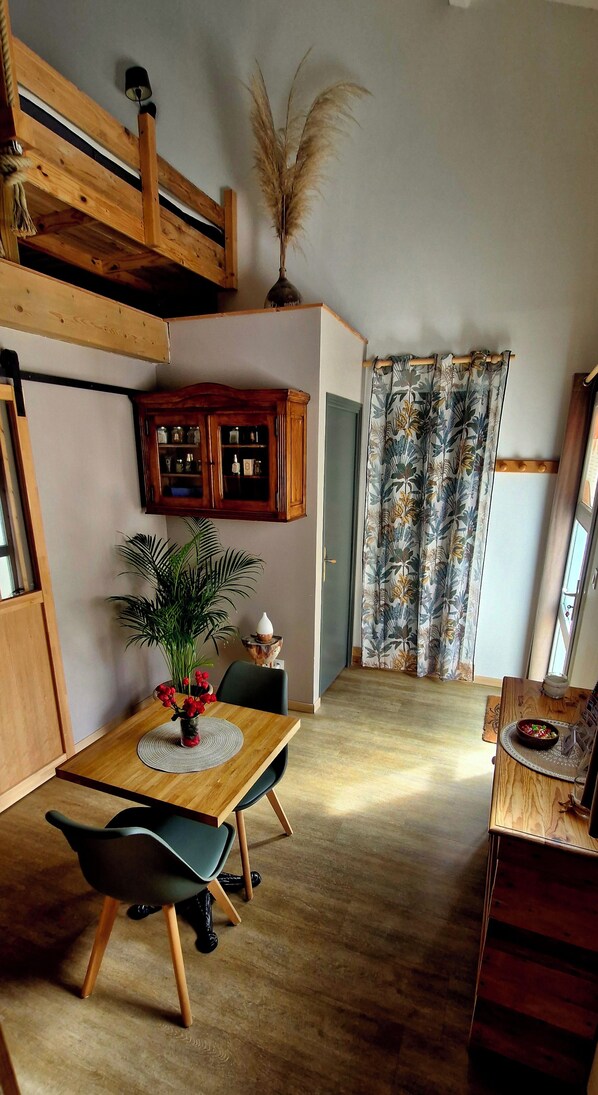 A dining area with a wooden table, chairs, a vase with flowers, a cabinet, and a window with curtains.
