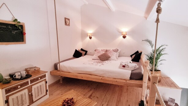 A cozy bedroom with a hanging bed, a small bedside table with a kettle, and a wall-mounted light fixture. - Suite with a private hot tub (Pierrelatte)