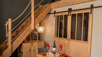 A wooden staircase with a rope railing leading to a loft area. A table with candles and a bottle of wine is set up in the lower level.