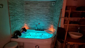 A bathroom with a stone wall, a bathtub, and a wooden shelf. - Suite with a private hot tub (Pierrelatte)