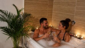 A couple in a hot tub with rose petals and candles, surrounded by a potted plant and a bottle of champagne. - Suite with a private hot tub (Pierrelatte)