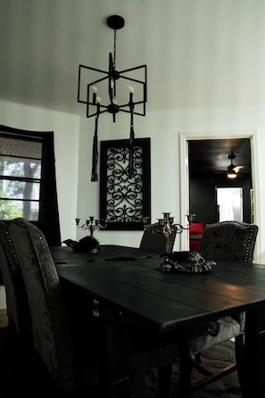 Uma sala de jantar com uma mesa de madeira escura, cadeiras pretas e um candelabro.