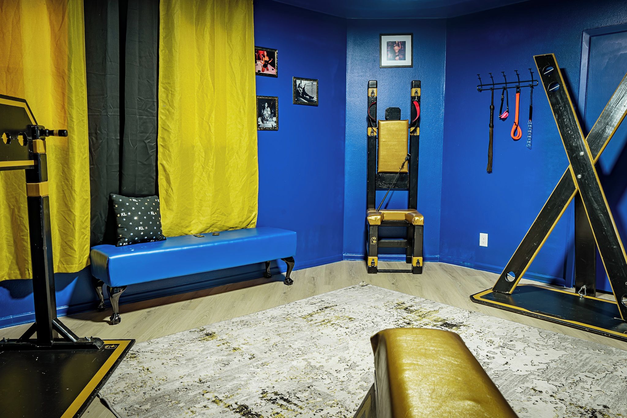 Een kamer met een blauwe wand, een blauwe bank, een geel gordijn, een trainingsapparaat in zwart en geel, en een trainingsbank in zwart en wit.